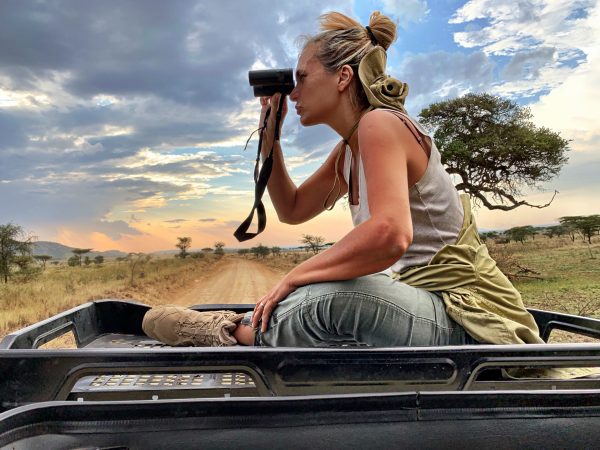 side-view-woman-looking-through-binoculars-while-sitting-car-roof-against-sky